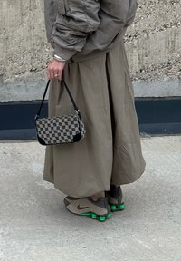 Small rectangular handbag made from patterned fabric in beige and black, matched with a long khaki skirt and grey Nike trainers featuring green accents.