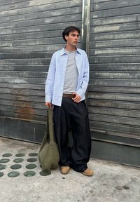 Šviesiai mėlynas ir baltas dryžuotas marškinėlių mygtukas ant pilkos marškiniai, derinamas su laisvomis juodomis kelnėmis. Laiko žalią pirkinių maišą, avėdamas kreminius sabo.