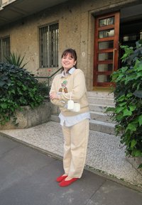 Beżowy sweter z haftem zwierząt, jasnoniebieska koszula w paski pod spodem, kremowe spodnie i czerwone baleriny, w połączeniu z małą białą torebką.