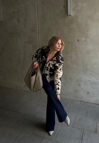 Μαύρο και κρεμ τζάκετ με σχέδιο αγελάδας, με μαύρη γιακά, συνδυασμένο με φαρδιά σκούρα τζιν και ανοιχτό γκρι ψηλοτάκουνα παπούτσια. Ψάθινη καφέ τσάντα.