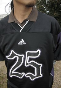 Czarna koszulka z brązowym kołnierzykiem, z dużą białą i purpurową cyfrą "25" z przodu, z logo Adidas powyżej.