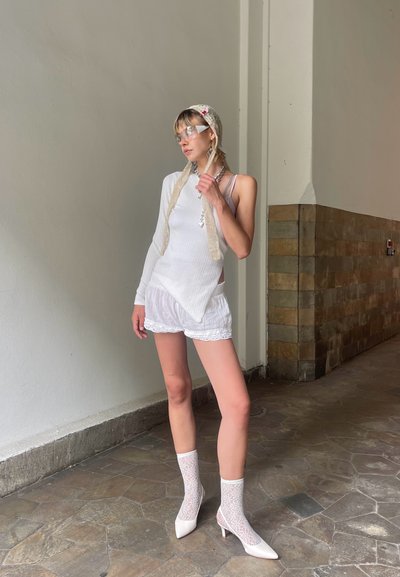 Top blanco de manga larga con costillas, pantalones cortos blancos transparentes con borde de encaje, calcetines blancos de red y tacones puntiagudos; accesorios incluyen un pañuelo de encaje para la cabeza.