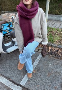 Palton gri supradimensionat cu nasturi negri, eșarfă de lână bordo, blugi albastru deschis, pantofi maro din piele întoarsă, ținând o geantă împletită maro închis.