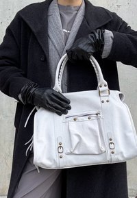 Hvid lædertaske med lynlåslomme, guldfarvede metaldetaljer og flettede håndtag; kombineret med sorte handsker og gråt overtøj.