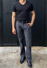 Zwarte v-hals t-shirt gecombineerd met grijze gestreepte broek en zwarte schoenen. De broek heeft een rechte snit en een subtiele textuur.