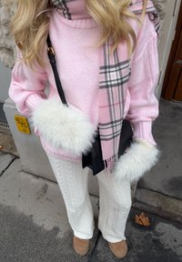 Pull tricoté rose pâle avec des poignets en fausse fourrure blanche, associé à un pantalon en maille torsadée blanc et une écharpe à carreaux rose. Sac bandoulière noir.