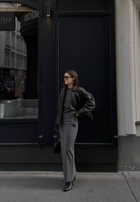 Melna ādas bomber jaka ar pelēku džemperi un augstu vidukli pelēku svārku, apvienota ar melniem potīšu zābakiem un melnām saulesbrillēm.