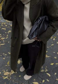 Ελαιόχρωμο μάλλινο παλτό, κρεμ ριμπ μπλ�ούζα, μαύρη δερμάτινη τσάντα με κορδόνια, μαύρο παντελόνι με ρίγες και ανοιχτόχρωμες φuzzy παντόφλες.