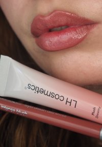 Glanzende naakte lipkleur op volle lippen, vergezeld van een lichtroze glansbuis met het label "Plush Dreamy" en een rode lippenpotlood.