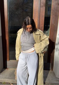 Trench bej, pulover gri tricotat și pantaloni sport gri deschis. Ținuta are o croială lejeră și texturi variate.