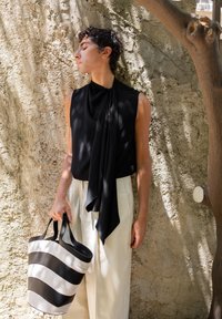 Nero top senza maniche con dettaglio annodato al collo, abbinato a pantaloni larghi di colore chiaro e una borsa a tracolla a righe bianco e nero.