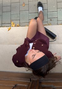 Jachetă burgundy cu două rânduri de nasturi aurii, bluză albă, bentiță neagră, loafers negri și ciorapi transparenți, așezată pe trepte din piatră.