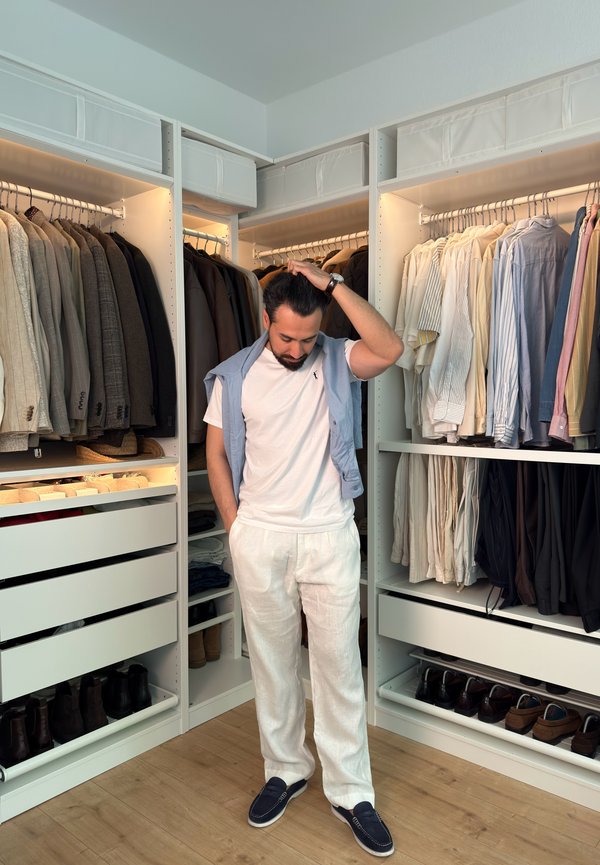 Mand står i en moderne walk-in closet med organiseret herretøj, sko og accessories omkring sig.