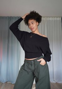 Schwarzer, schulterfreier Pullover mit geripptem Bund, kombiniert mit lockeren, olivgrünen Hosen mit Kordelzug und Seitentaschen.