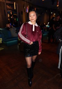 Camisa de manga larga de terciopelo granate con cuello blanco y tres rayas blancas; minifalda ajustada de lentejuelas negra; tacones negros hasta la rodilla.