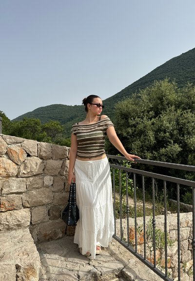 Top sin tirantes de punto a rayas marrón y blanco, combinado con una falda larga blanca y fluida. Accesorios incluyen un bolso negro y gafas de sol.