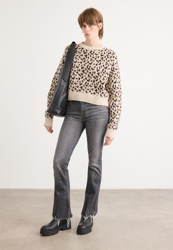 Beiger Pullover mit schwarzen Leopardenflecken, gerippter Ausschnitt, kombiniert mit dunkelgrauen, ausgestellt geschnittenen Jeans mit fransigen Säumen und schwarzen, klobigen Stiefeletten.