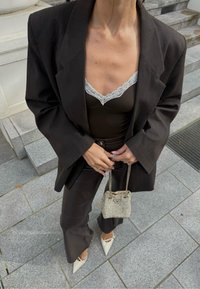 Donker gestreepte oversized blazer over een bruine top met kantafwerking, gecombineerd met bruine uitlopende broeken, witte puntige schoenen en een zilveren tas.
