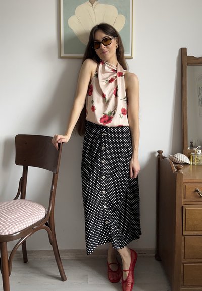 Top de flores tipo halter en rosa claro, combinado con una falda midi negra con lunares y botones en la parte delantera; unos zapatos rojos de malla tipo slip-on completan el conjunto.