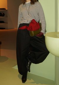 Haut à manches longues rayé, pantalon noir ample, sac à main rouge avec un nœud, et bottines noires à bout pointu. Textures remarquables et couleurs contrastées.