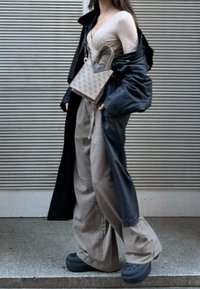 Femme portant un haut cache-cœur beige, un pantalon rayé à jambes larges, un manteau noir surdimensionné, des chaussures noires sans lacets, et portant un sac à main beige à motif.