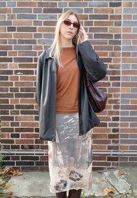Black leather jacket, brown top, sheer floral-printed skirt, brown handbag. Accessories include oval sunglasses and textured tights.