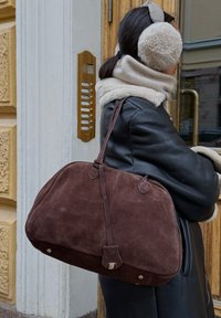 Sac à main en daim marron avec une silhouette arrondie, deux courtes anses, des coutures visibles et des accents de quincaillerie de couleur argentée.