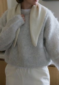 Pull gris clair en tissu duveteux avec un col blanc posé sur les épaules. Le pull est ample avec des poignets côtelés, porté avec un pantalon blanc.