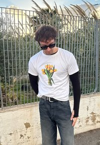 Λευκή μπλούζα με γραφικό μπουκέτο κίτρινων τουλιπών, μαύρο μακρυμάνικο πουκάμισο από κάτω, μαύρη ζώνη με καρφιά και σκούρα τζιν.