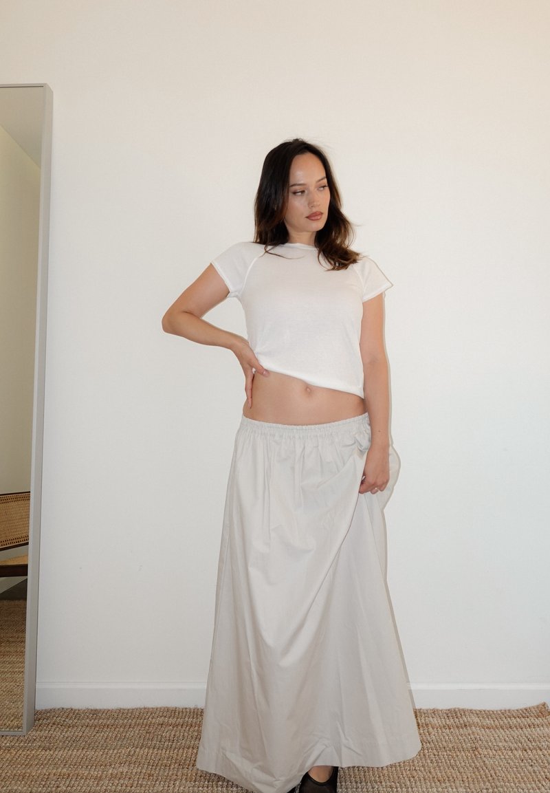 Λευκό κοντομάνικο cropped t-shirt συνδυασμένο με μια ανοιχτή μπεζ φούστα maxi με ελαστική μέση, η οποία διαθέτει λεία υφή και χαλαρό, ρέον σχέδιο.