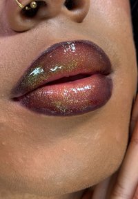 Błyszczące usta z efektem ombre, przechodzące od głębokiego śliwkowego koloru do błyszczącego różu z złotym połyskiem; skóra jest gładka z subtelnymi detalami tekstury.