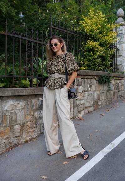 Top de peplum con estampado de leopardo y mangas abullonadas, combinado con pantalones de pierna ancha en beige claro. Bolso de mano negro y sandalias de tacón. Entorno al aire libre.