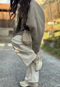 Svetlosivý predimenzovaný blejzer, biely šál, khaki široké nohavice a béžové tenisky. Malá kovová kabelka so sťahovacím detailom.