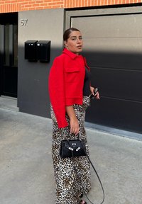 Rød tekstureret jakke, tætsiddende sort top og leopardmønstret nederdel. Sort håndtaske med kædetræk. Ensfarvet sort baggrund og urban setting.