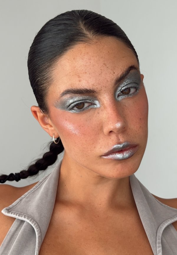 Femme aux cheveux tressés, fard à paupières métallique argenté et rouge à lèvres, portant un haut gris clair sans manches sur un fond uni.