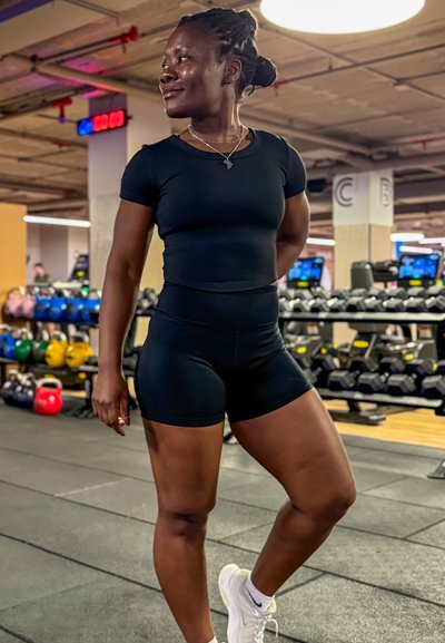 Conjunto deportivo negro que consta de una camiseta ajustada de manga corta y pantalones cortos de cintura alta; textura suave; persona en un gimnasio.