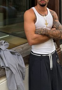 Un débardeur blanc sans manches et un pantalon plissé noir avec un cordon blanc. Une chemise à carreaux légère est drapée à côté d'une surface en bois.