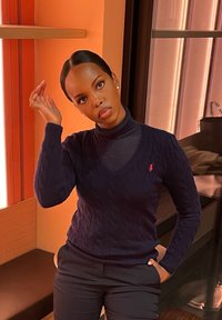 Laivastonsininen palmikkoneulottu neulepaita V-kaula-aukolla ja pitkillä hihoilla, yhdistetty tummiin housuihin. Päällä on yksinkertaiset hopeiset korvakorut.