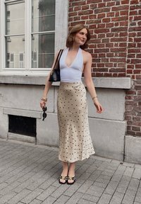 Hvit halterneck topp med dyp utringning, beige satenskjørt med svarte prikker, svart veske og svarte sandaler med blomsterdetaljer.