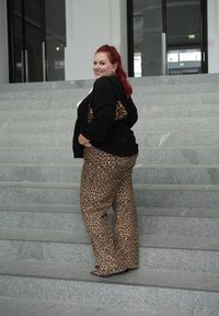 Παντελόνι φαρδύ με λεοπάρ τυπώματα και μαύρη peplum μπλούζα. Το μοντέλο κρατάει μια τσάντα χειρός με λεοπάρ τυπώματα, στέκεται σε λιθόστρωτα σκαλιά.