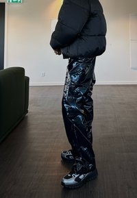 Puffete svart jakke med en glansfull finish, kombinert med skinnende svarte bukser og kraftige grå sneakers. Glatte teksturer og sterke farger.