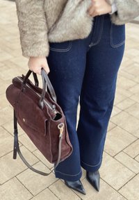 Braune Wildleder-Handtasche mit Ledergriffen, Reißverschluss und Fronttasche. Kombiniert mit dunkelblauen Schlagjeans und schwarzen spitzen Absätzen.