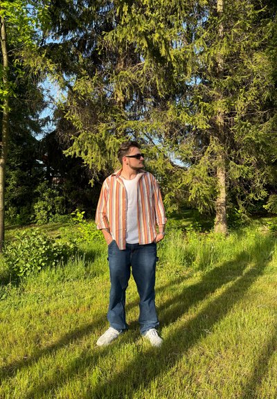 Camisa de botones a rayas en naranja, blanco y amarillo, combinada con pantalones de mezclilla azul. Se lleva con zapatillas blancas y gafas de sol, al aire libre.