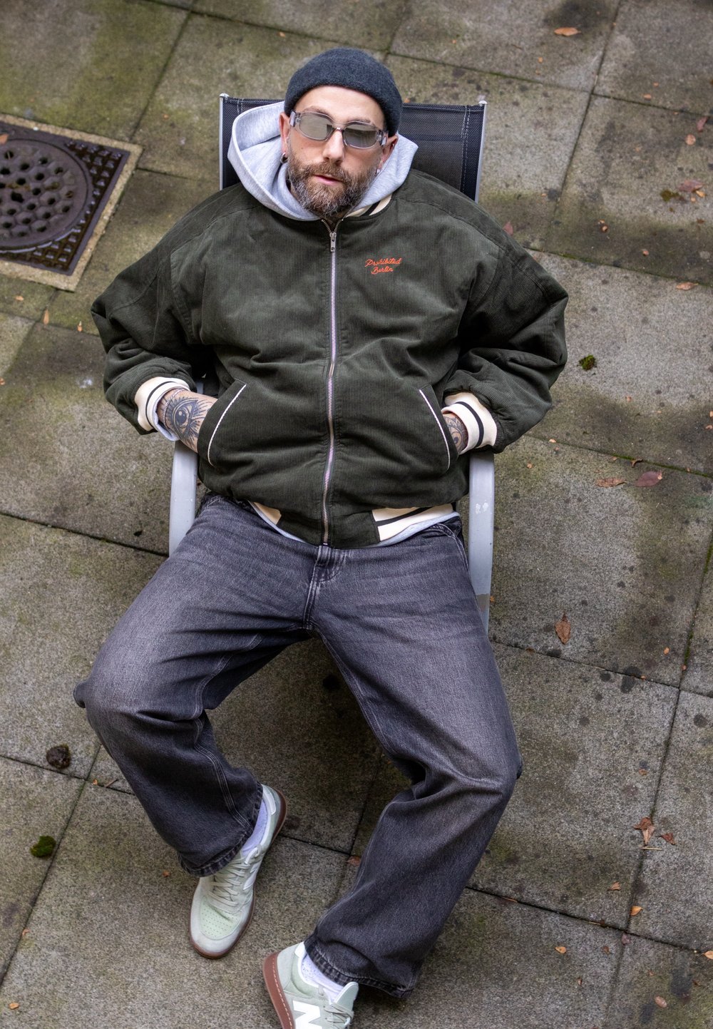 Veste bomber en velours côtelé vert avec des poignets blancs, jean gris, et baskets vert clair. La personne est assise sur une chaise en plein air.