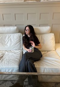 Divano bianco in pelle con superficie texturizzata, tavolo in vetro, persona con maglietta nera e pantaloni a righe che tiene una tazza chiara, posa rilassata.