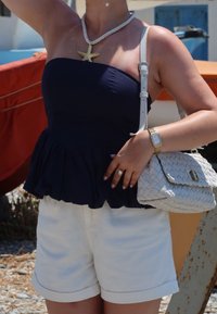 Ναυτικό peplum τοπ από βαμβάκι με κολιέ από αστερία; κρεμ σορτσάκια από βαμβάκι με διπλωμένα τελειώματα; πλεκτή λευκή τσάντα με κούμπωμα.