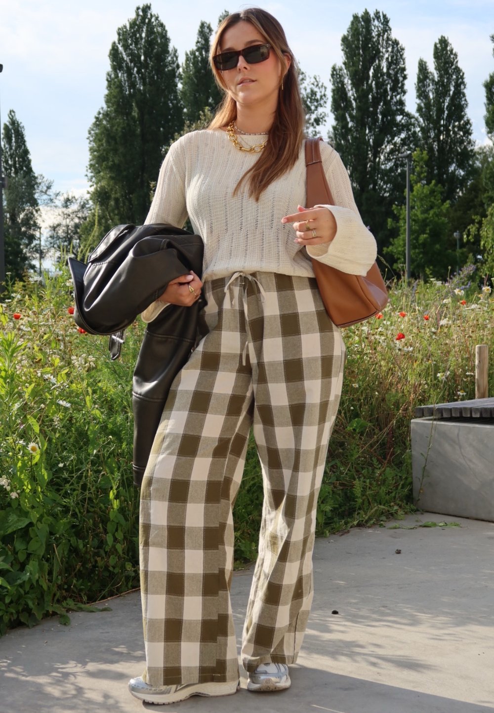 Μπατζάκια φαρδιά με καρό σχέδιο σε πράσινο και κρεμ, συνδυασμένα με ένα ελαφρύ κρεμ πλεκτό πουλόβερ και μια μαύρη δερμάτινη τζάκε�τ.