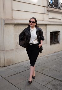 Zwarte leren jas over een witte top, gecombineerd met zwarte cropped broek en bruine hakken. Een bruine tas maakt de look compleet. Buiten locatie.