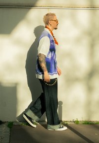 Nadměrná košile s krátkými rukávy s modrým grafickým motivem, v kombinaci se širokými tmavými džínovými kalhotami a černými teniskami s bílými podrážkami.