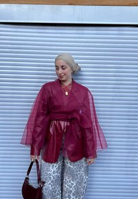 Bluzka w kolorze bordowym z warstwami i przejrzystymi rękawami, zestawiona z szerokimi spodniami w panterkę. Dodatkiem jest mała bordowa torebka.